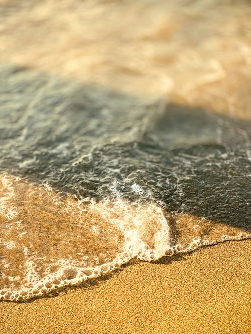 Free Captivating close-up of waves softly crashing onto a sandy beach, capturing a serene coastal moment. Stock Photo