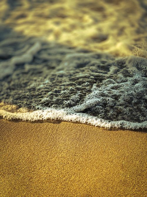 Free Close-up of ocean waves softly lapping on a sandy beach under warm sunlight. Stock Photo