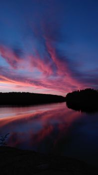 Stunning sunset with pink clouds reflecting in a serene Finnish lake.