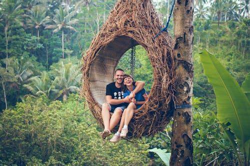 Мужчина и женщина сидят на подвесном стуле у дерева