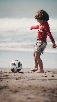 Young child plays with a soccer ball on a sunny beach, enjoying summer fun.