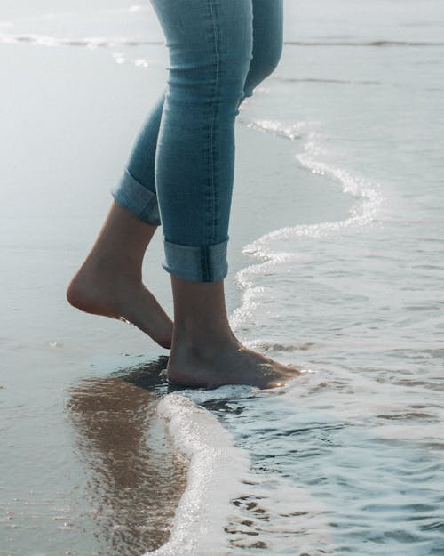 A Person in Blue Denim Jeans Standing on Beach Shore