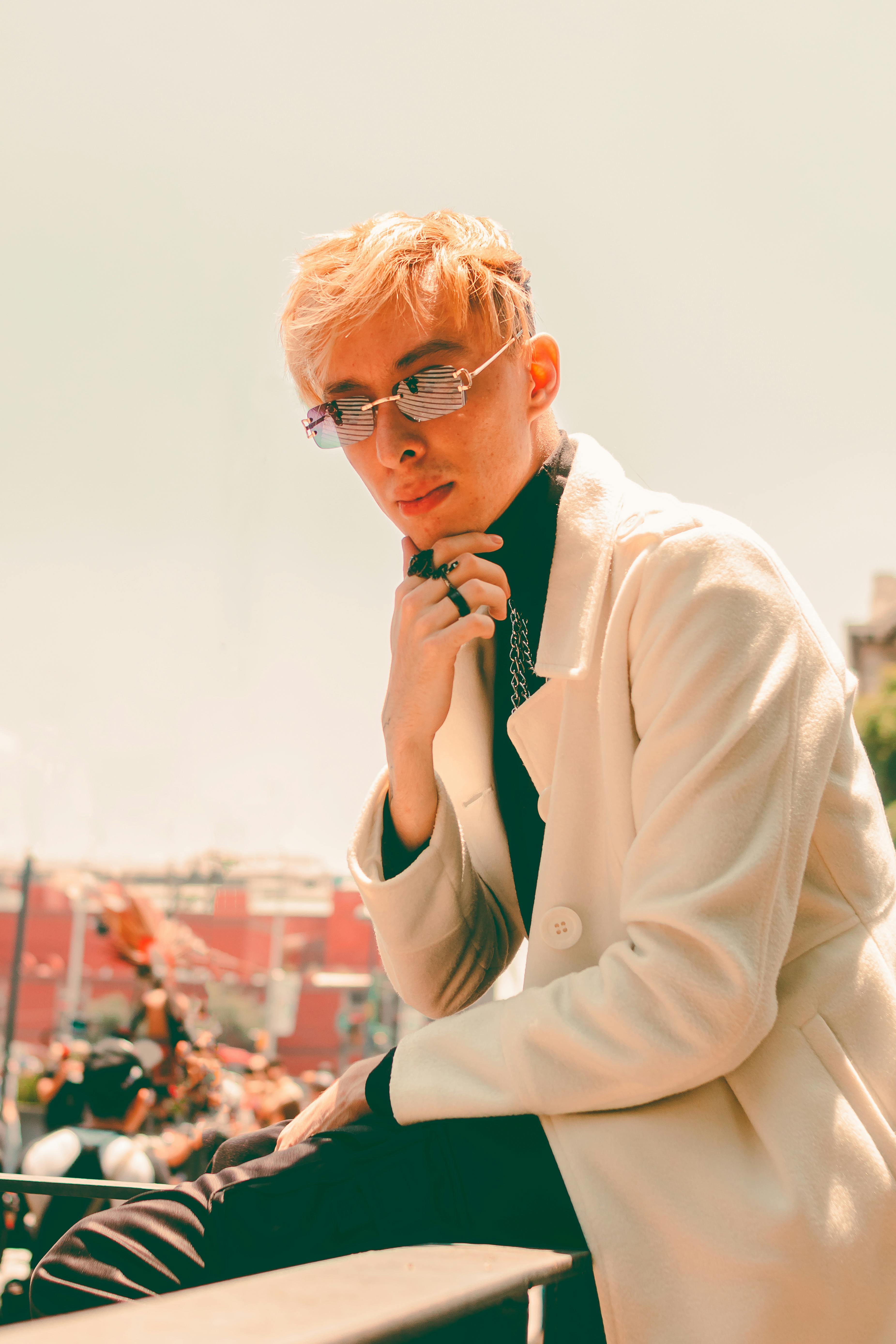 Fashionable young adult with blonde hair posing outdoors in stylish sunglasses and white coat in Mexico City.