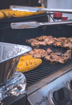 Close-up of grilled corn and chicken on an outdoor barbecue grill.