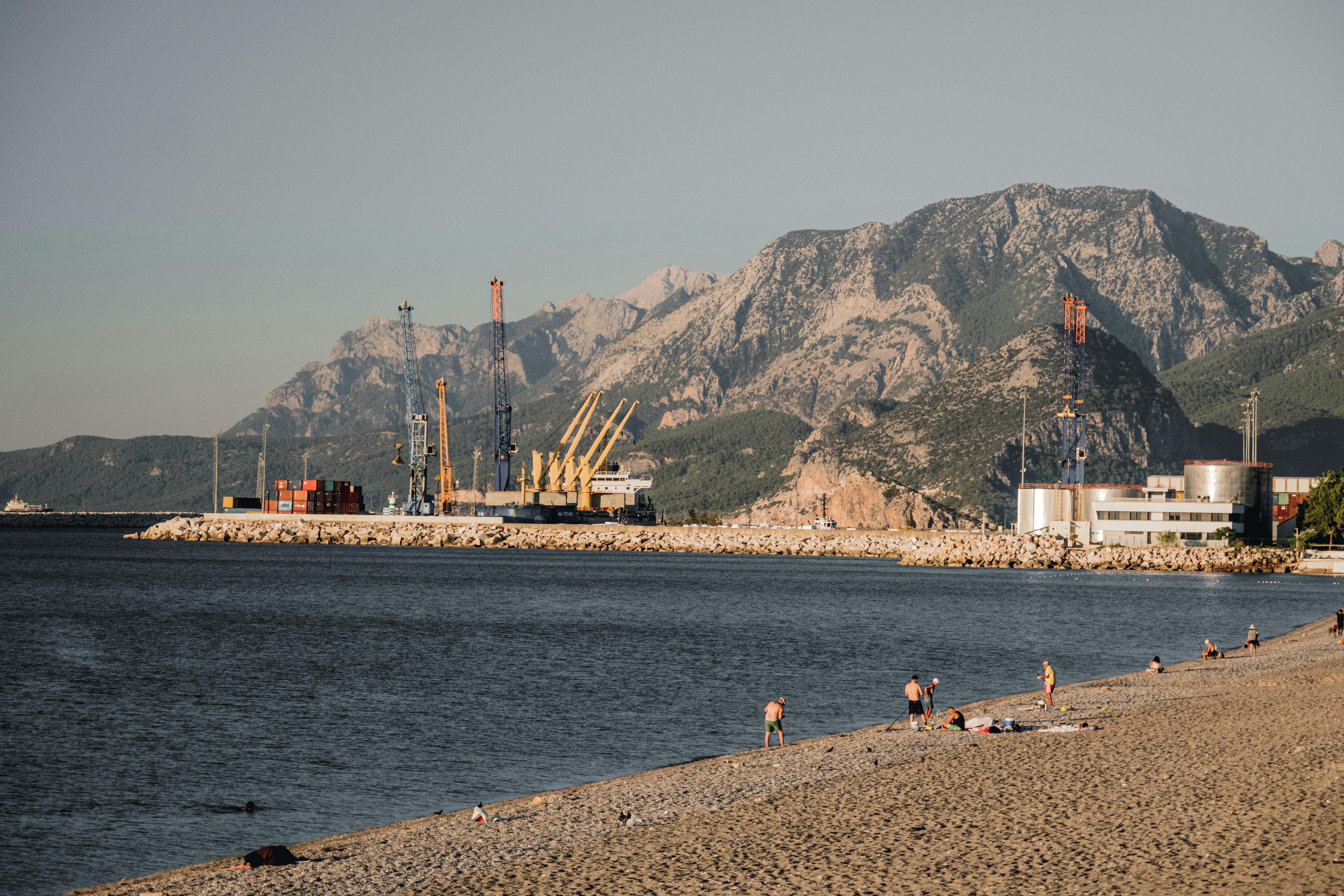 A picturesque coastal scene featuring a harbor, mountains, and sunbathers.