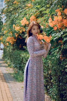白天，一位身穿花卉连衣裙的亚洲女子在充满活力的花园里摆姿势