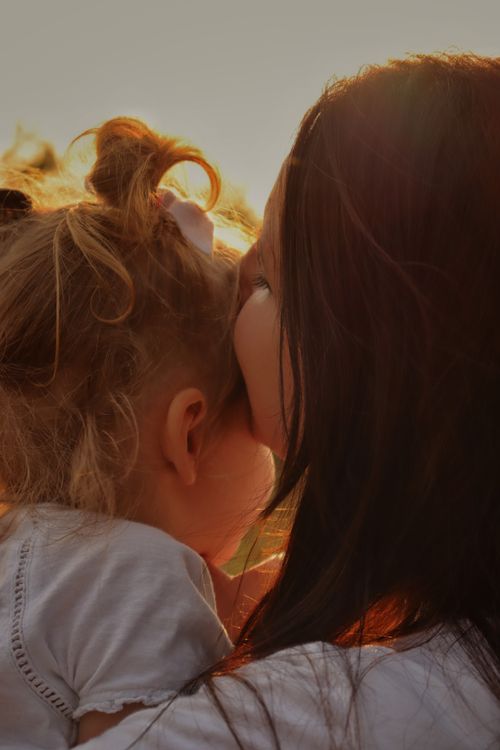 Free A heartwarming close-up of a mother kissing her young daughter outdoors during sunset. Stock Photo