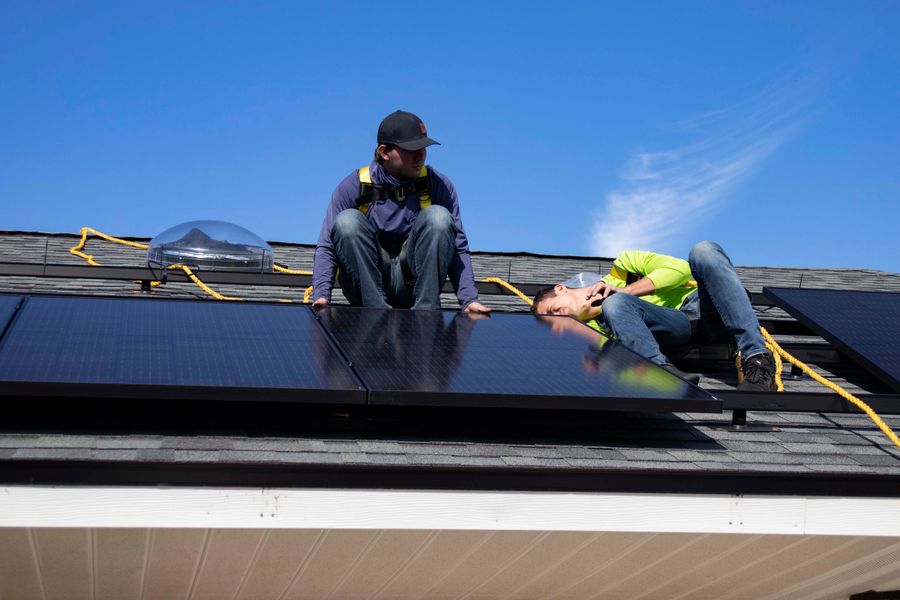 Workers installing solar panels on a rooftop in St. Augustine under clear skies.