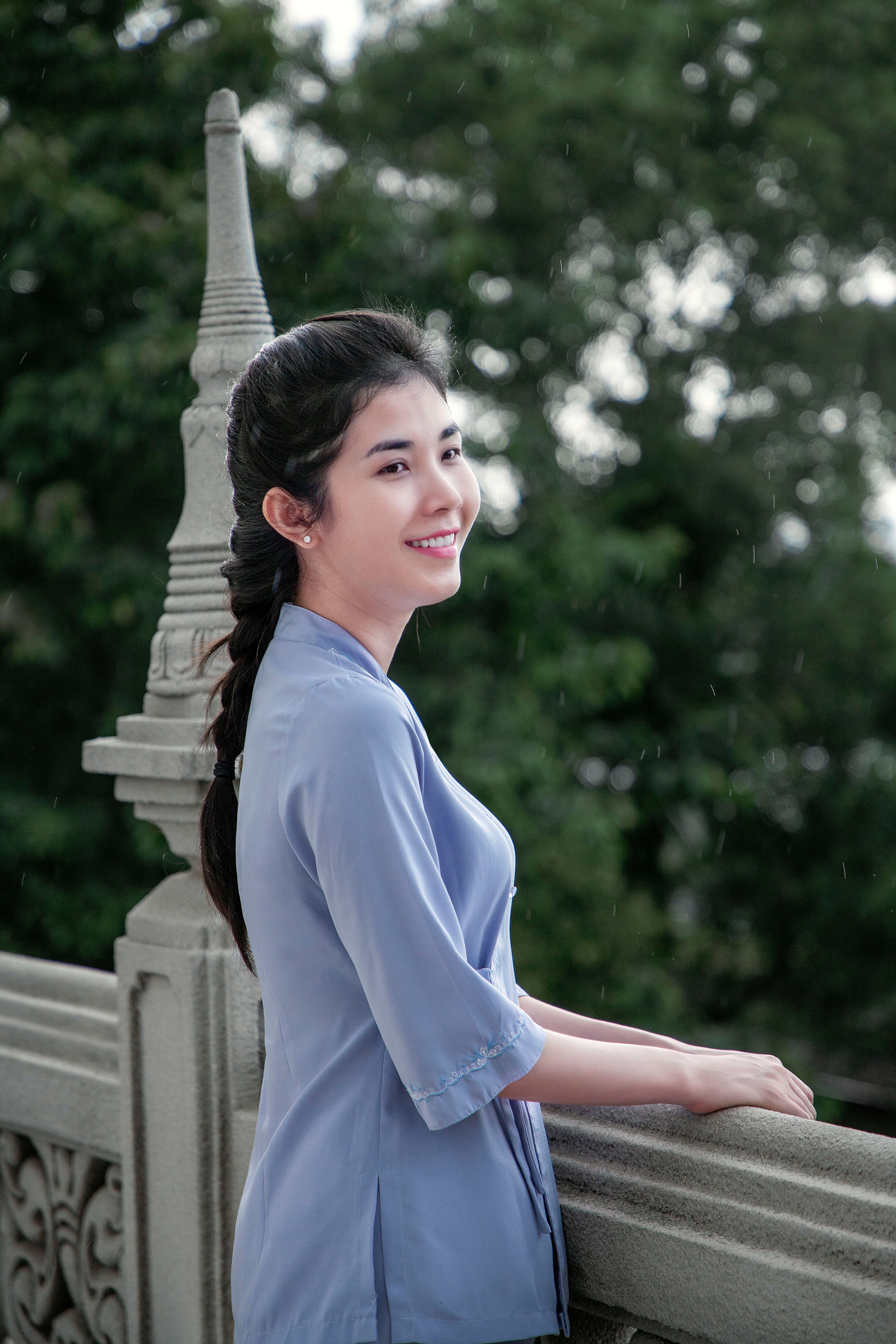 Young woman with braided hair smiling outdoors in a blue dress.