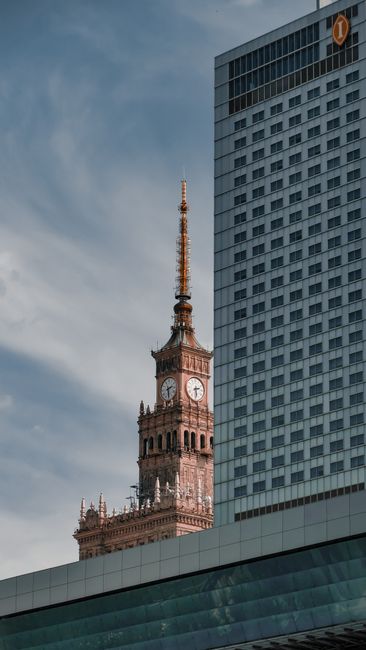 Vertical view of Warsaw's iconic Palace of Culture and Science clock tower against modern architecture.