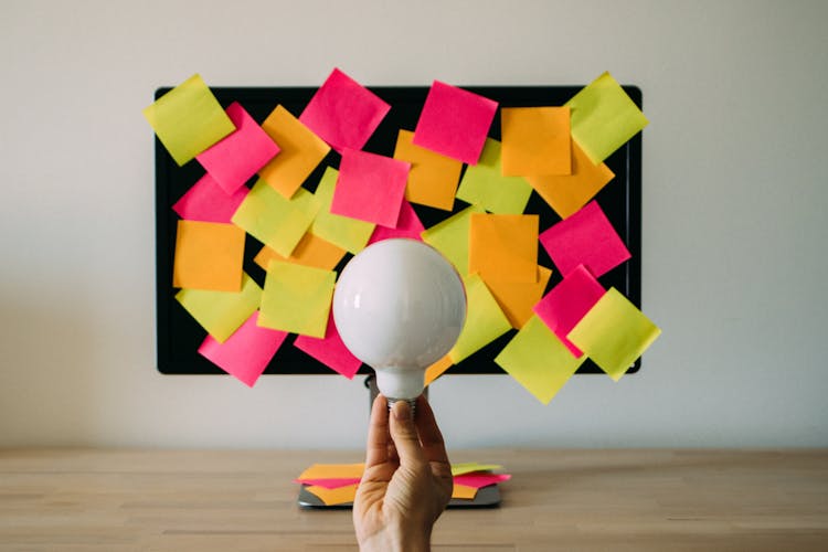 Hand Holding A Light Bulb Against A Board With Sticky Notes