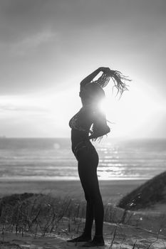 Striking black and white silhouette of a woman standing on the beach at sunset, emphasizing elegance and tranquility.