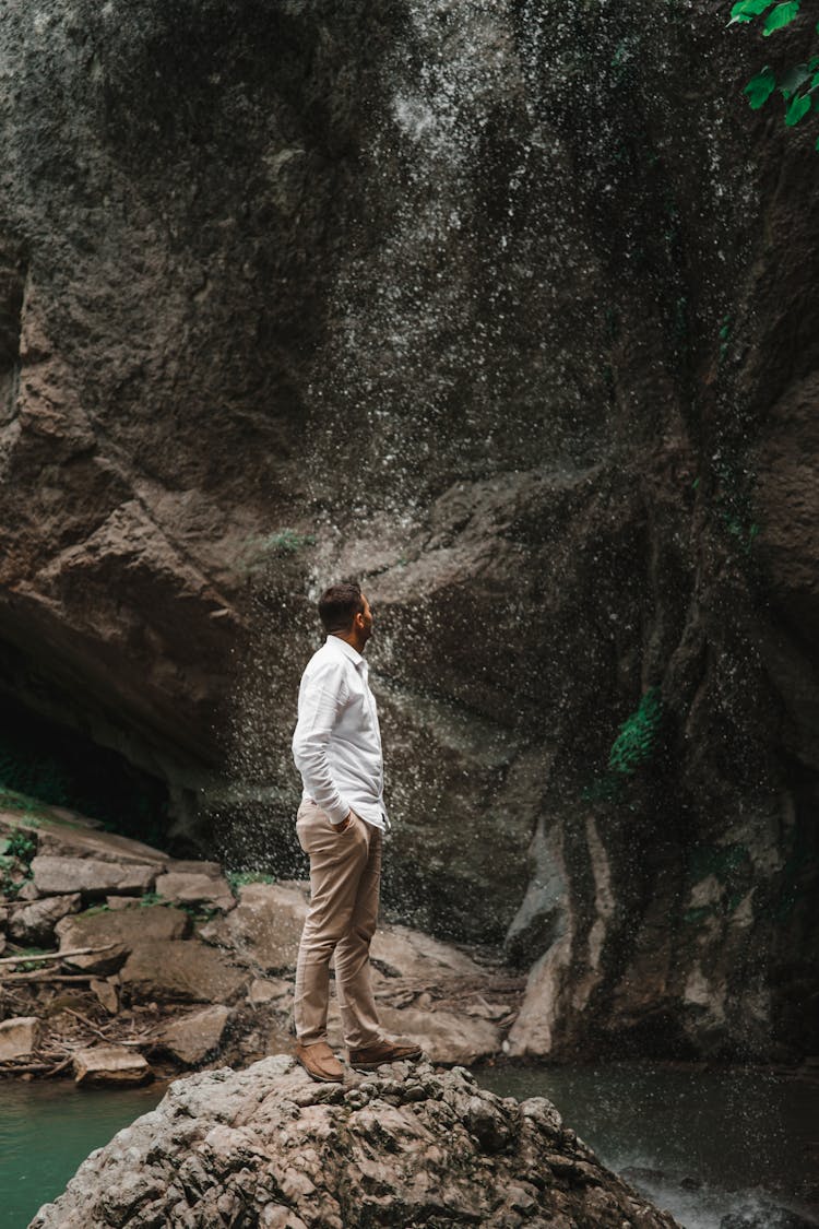 Man Standing On Rock Near Waterfall