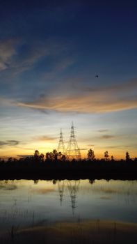 A tranquil scene of transmission towers silhouetted against a vibrant sunset, reflecting in calm water.