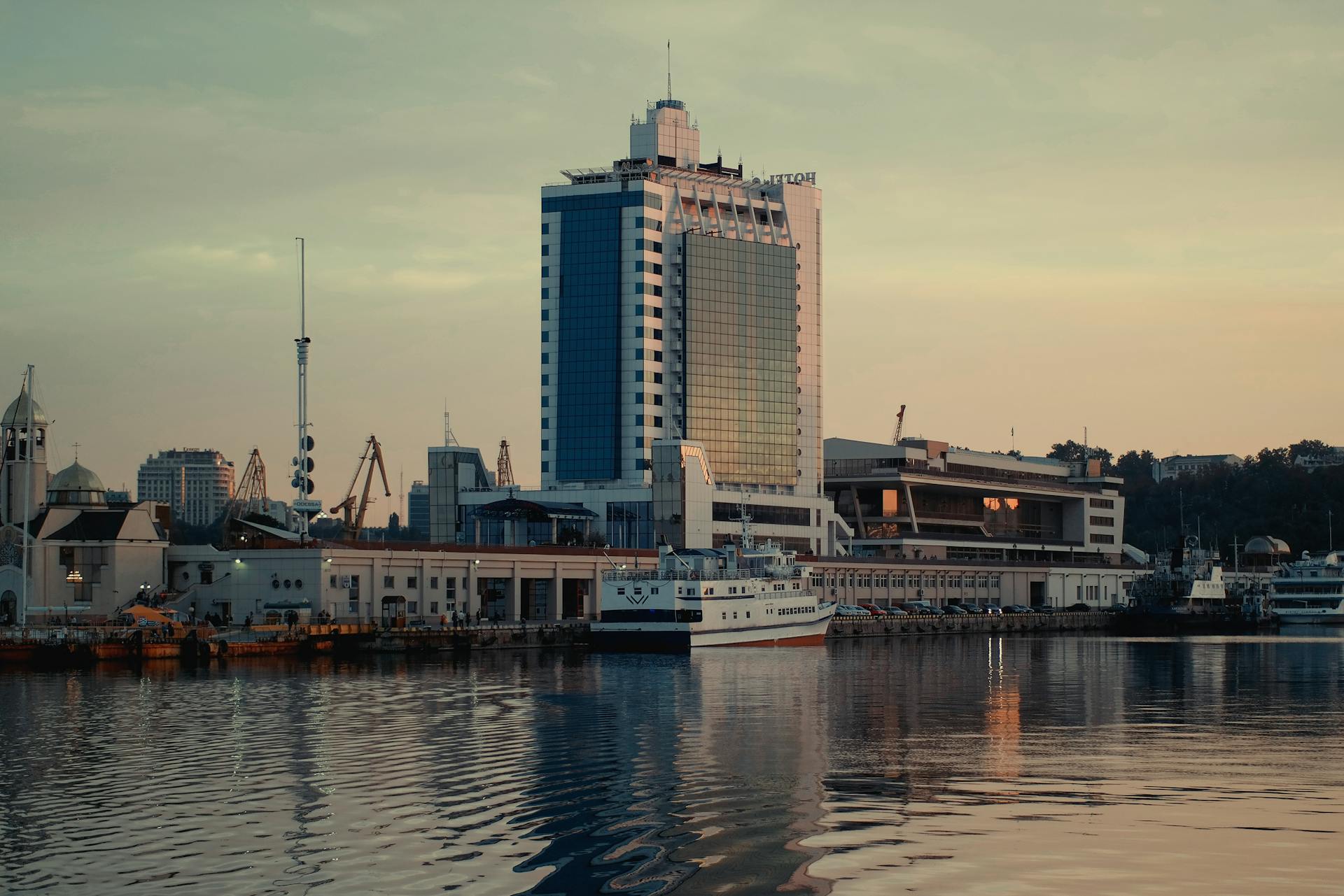 Scenic view of Odesa Sea Port and modern architecture reflecting in water during sunset.