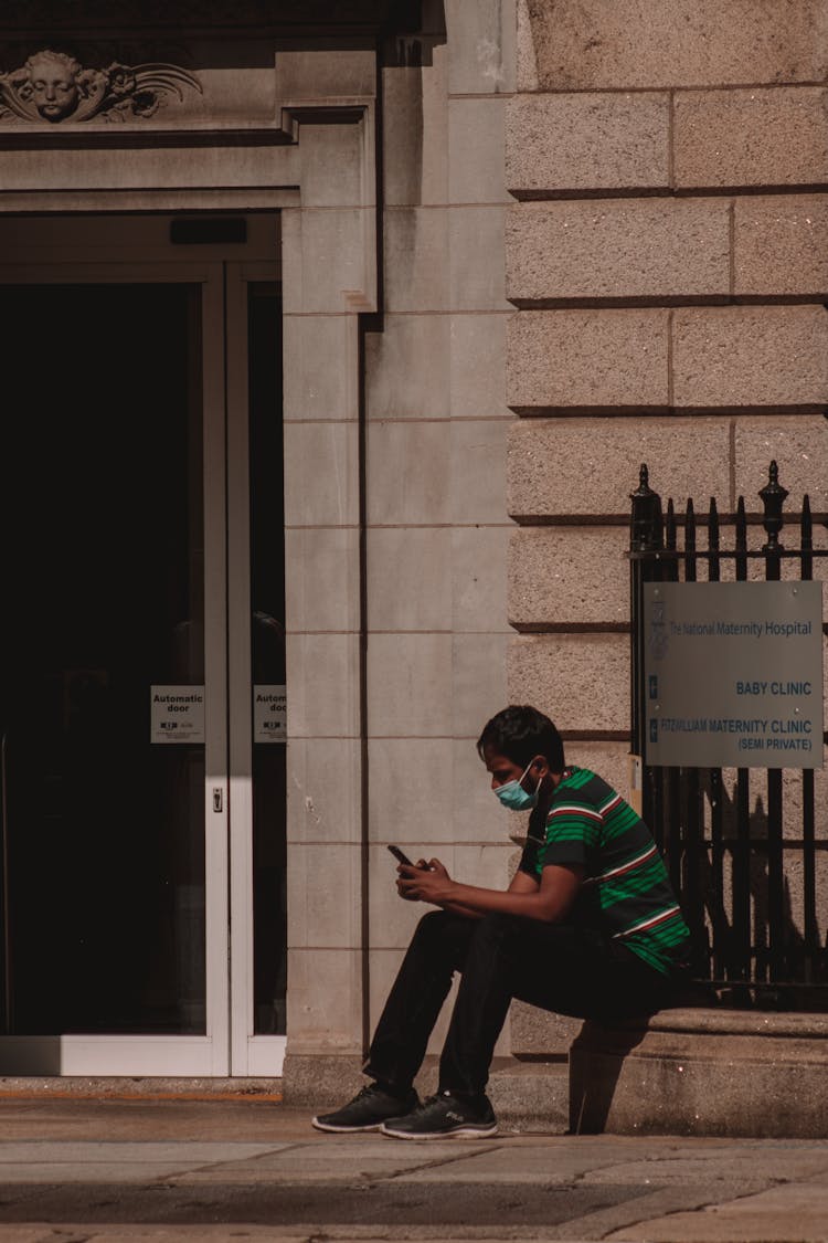 Man In Face Mask Using Smartphone On Sidewalk