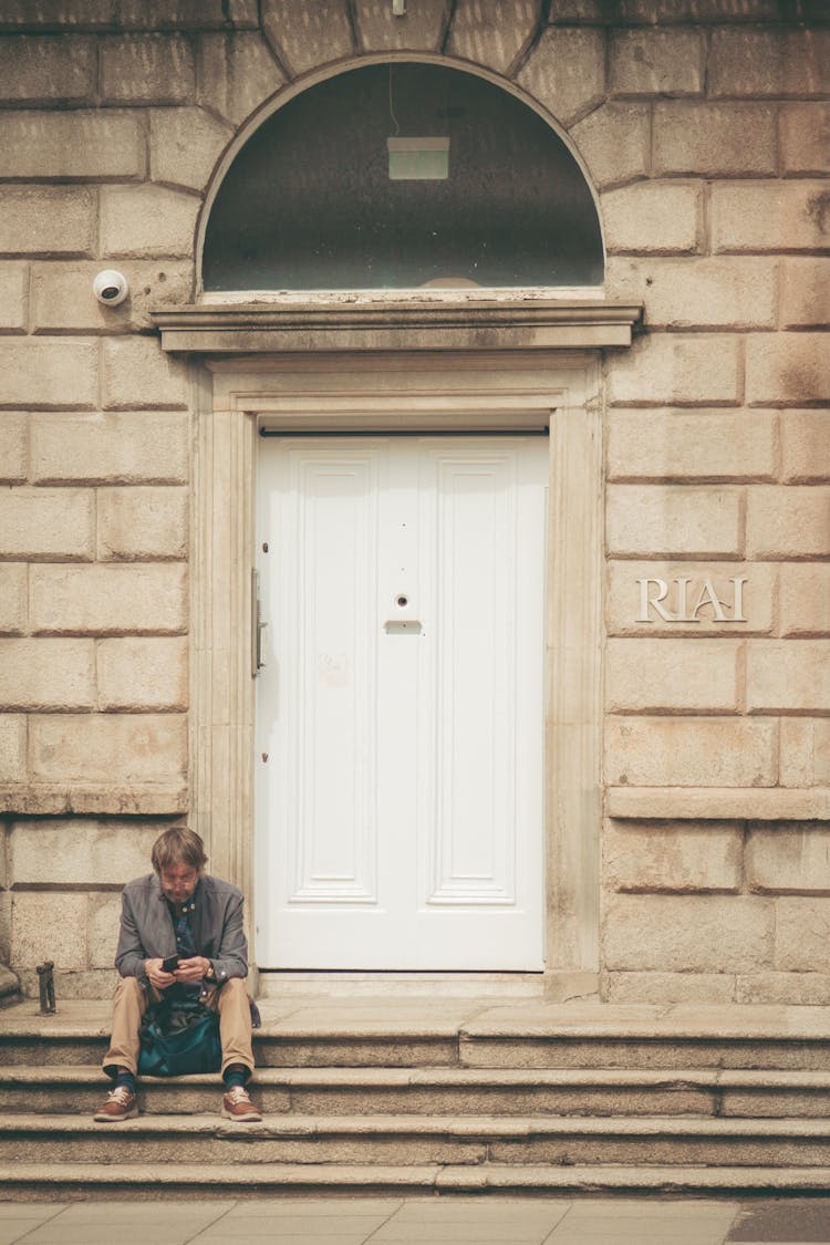 Man Sitting On Stairs Near Stone Building