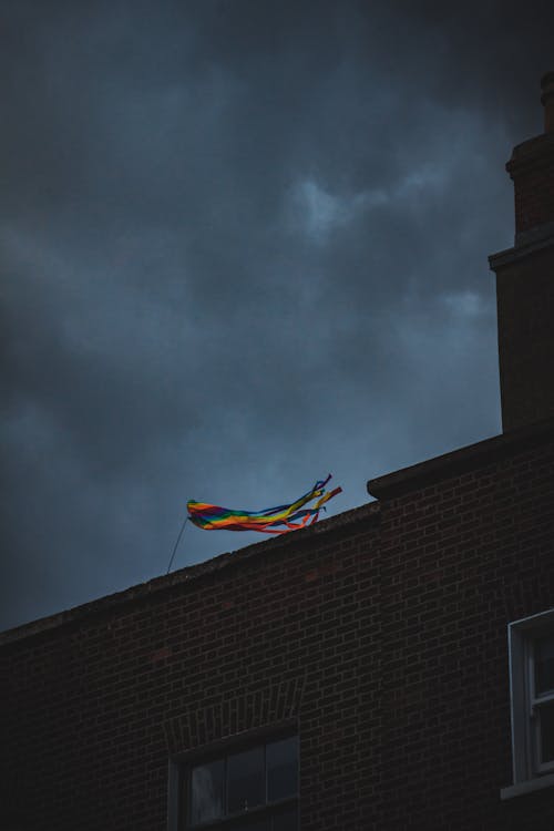 A Rainbow Flag on Rooftop Under Gray Clouds
