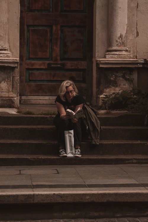 Free A woman sits reading a book on stone steps outside an old door in Dublin, Ireland. Stock Photo