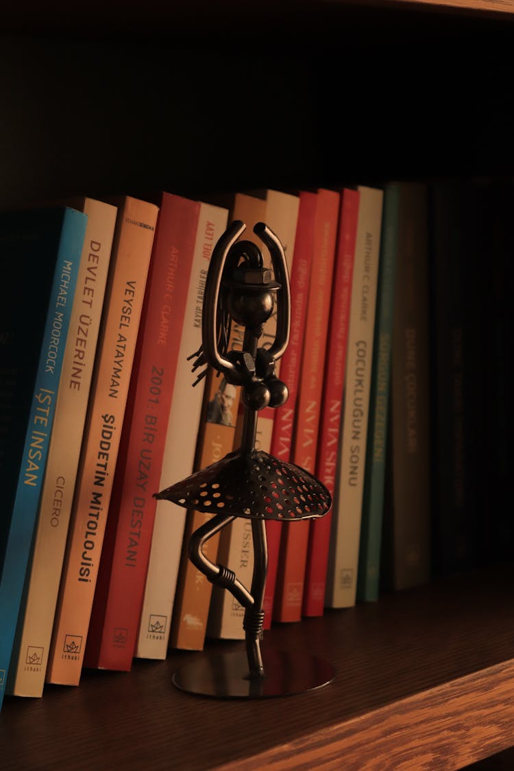 A Metal Ballerina Figurine Near The Books 