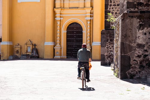 A Back View of a Man in Gray Shirt Riding a Bike on the Street