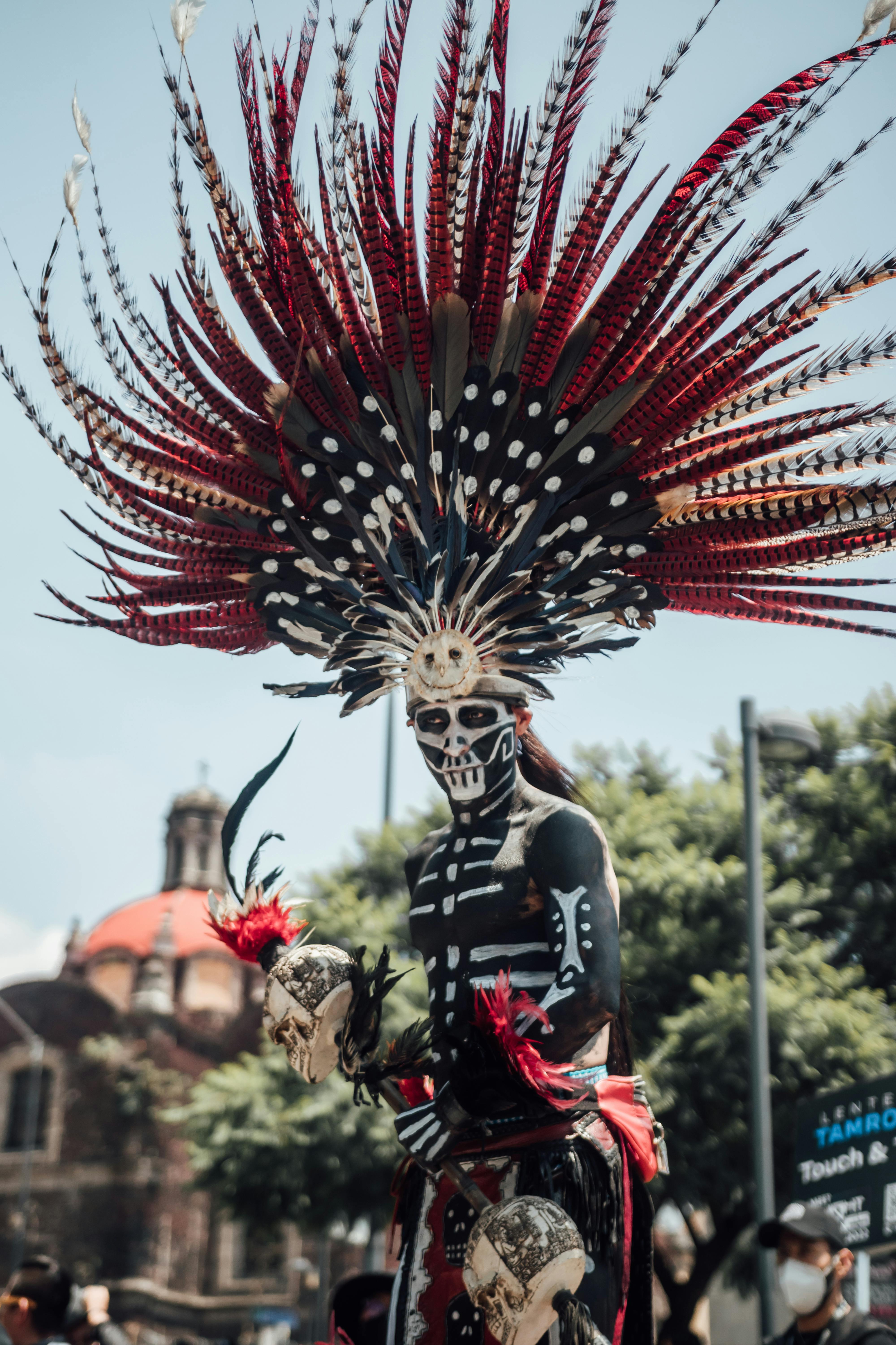 Traditional Aztec attire with feather headdress at Mexico City's Día de los Muertos celebration.