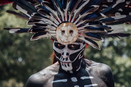 Close-up portrait of a person wearing traditional Mexican makeup and feather headdress outdoors.