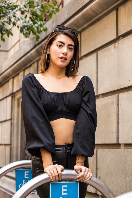 Free Fashionable young woman in a black crop top and hoop earrings posing confidently against an urban backdrop. Stock Photo