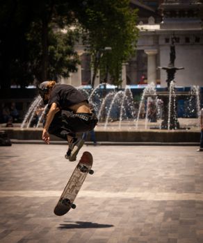 Skater in mid-air performing a trick near a water fountain in a bustling city park.. skater, performing, trick