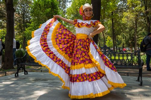 Free Woman in traditional Mexican dress smiling in a sunlit park, surrounded by greenery. Stock Photo