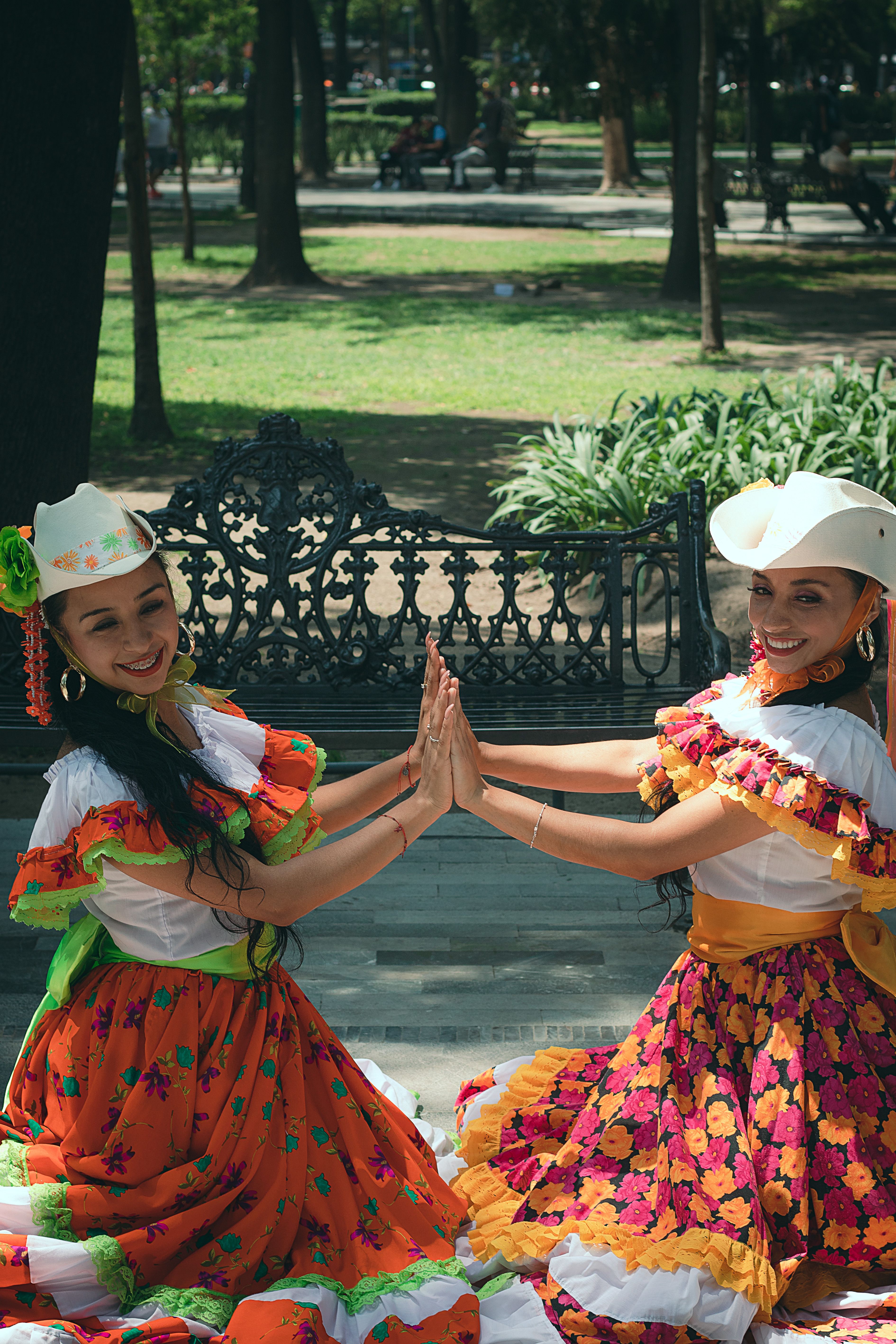 Fotomural Dos mujeres con vestidos y sombreros florales vibrantes disfrutando de un día soleado al aire libre.
