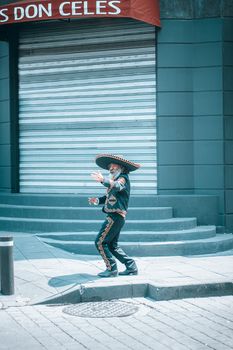 A street performer in traditional Mexican clothing dances on a city sidewalk.