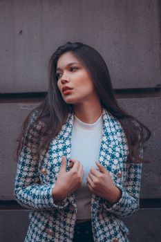 Portrait of a fashionable woman in a blue and white coat posing against a textured stone wall.