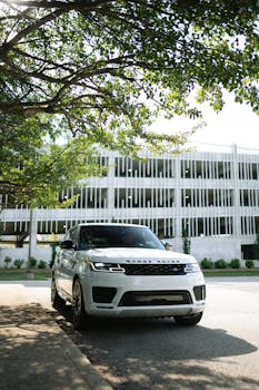 A white Range Rover SUV parked under a tree near a modern building.