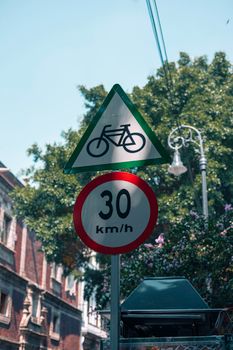 Street signs for bicycles and speed limit in Ciudad de México, surrounded by urban trees.