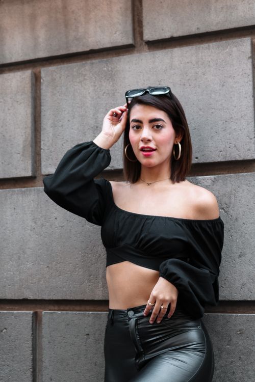 Free Fashionable adult woman wearing sunglasses and a black off-shoulder top standing against a concrete wall. Stock Photo