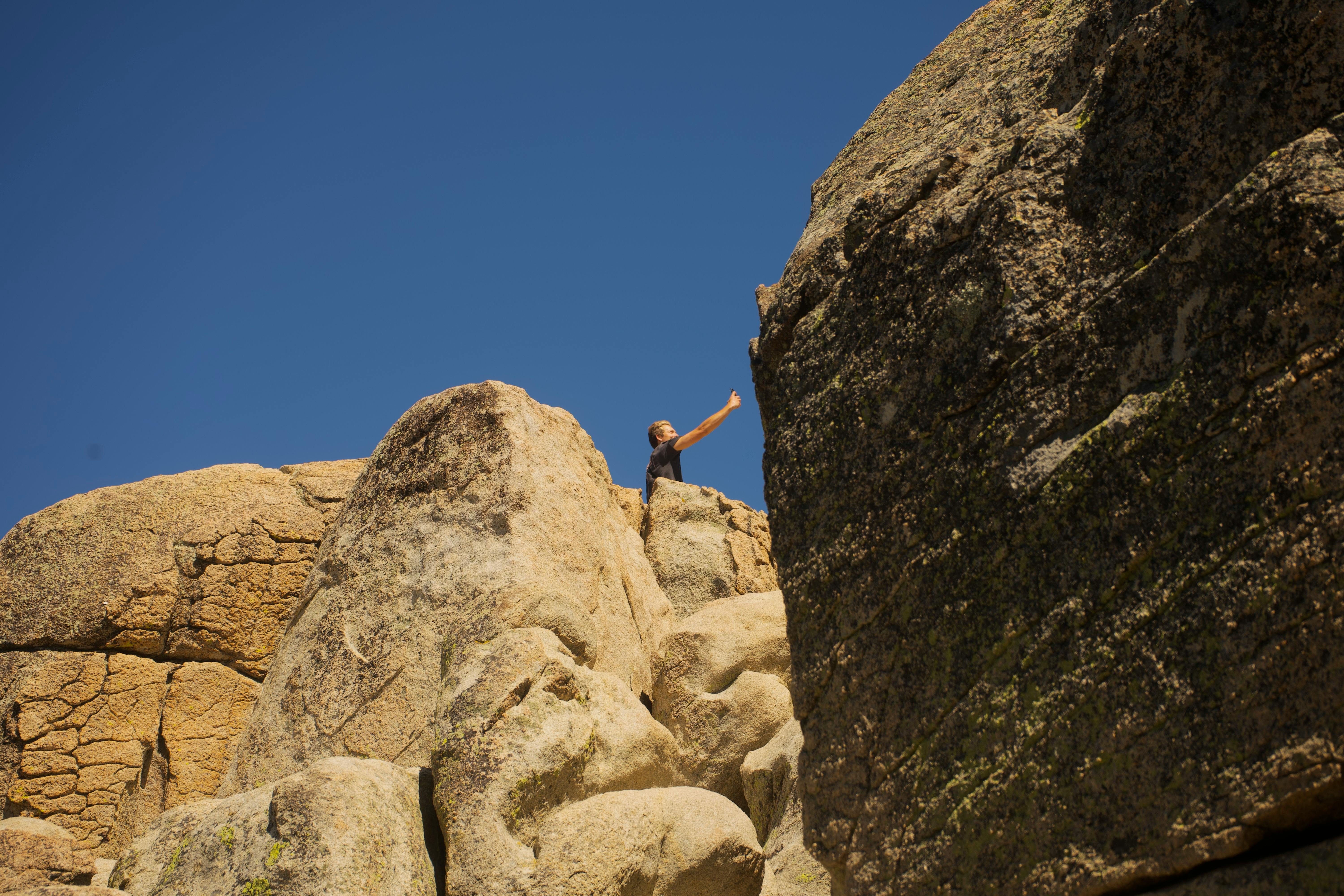 A person reaches the top of a rugged cliff under a clear blue sky, symbolizing achievement.