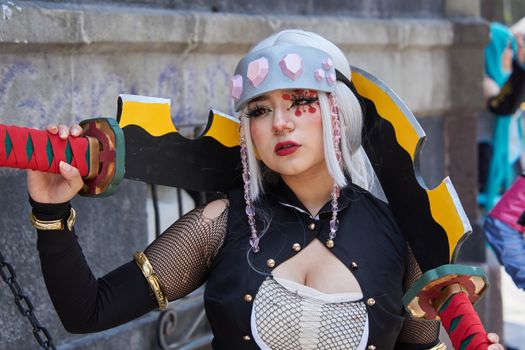 A woman in fantasy cosplay with creative makeup holding a large sword outdoors.