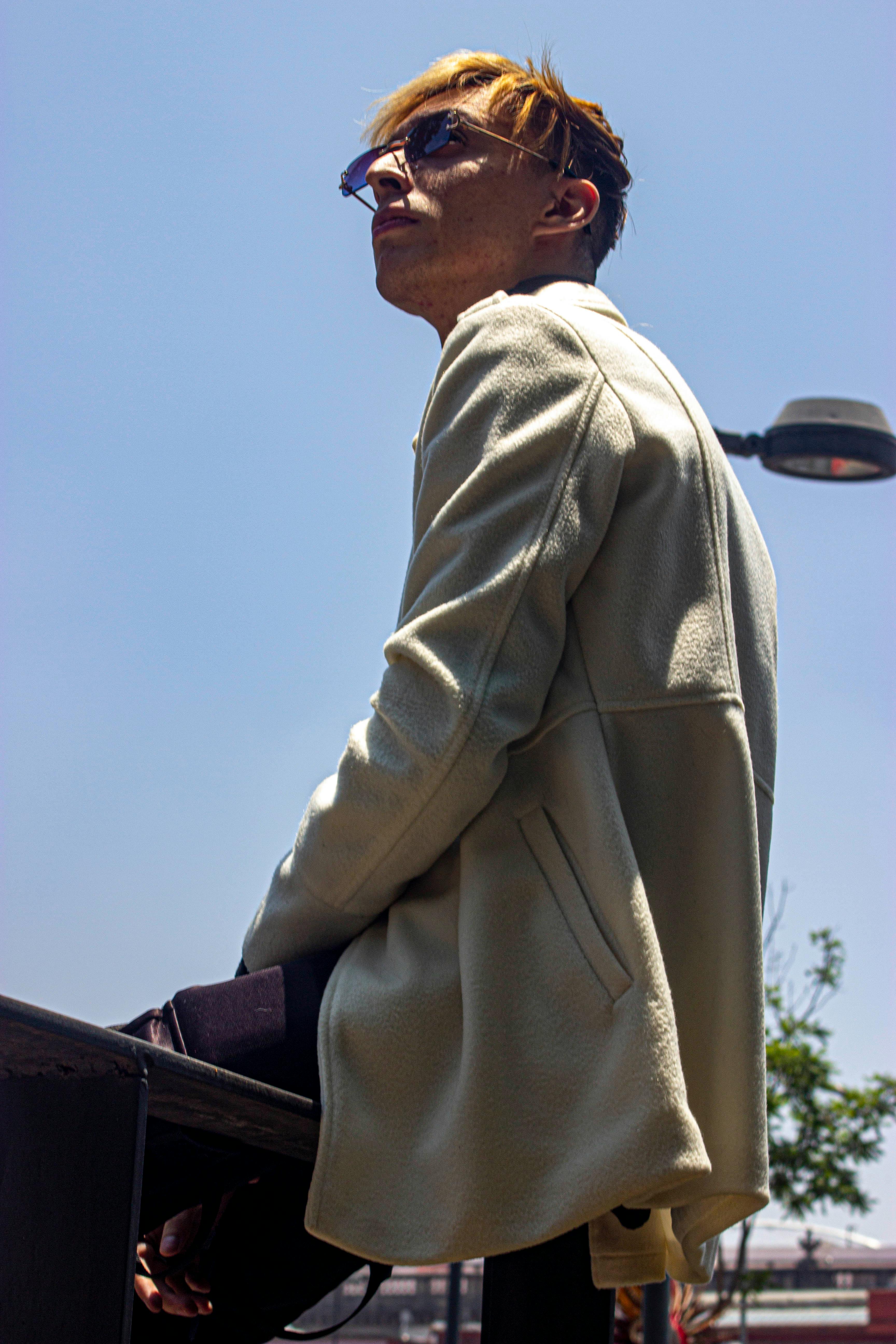 Young man in sunglasses sitting outdoors under a bright sky.