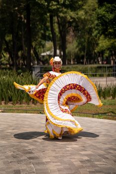 A woman performing traditional Mexican folkloric dance in a colorful dress outdoors.