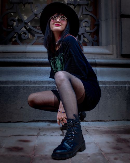 Free Stylish woman squatting in front of ornate wall, wearing edgy outfit with boots and sunglasses. Stock Photo