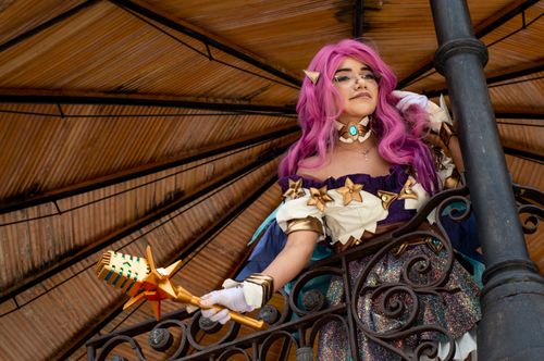 Free A captivating cosplay character with pink hair and detailed costume holding a magical wand on a decorated balcony. Stock Photo