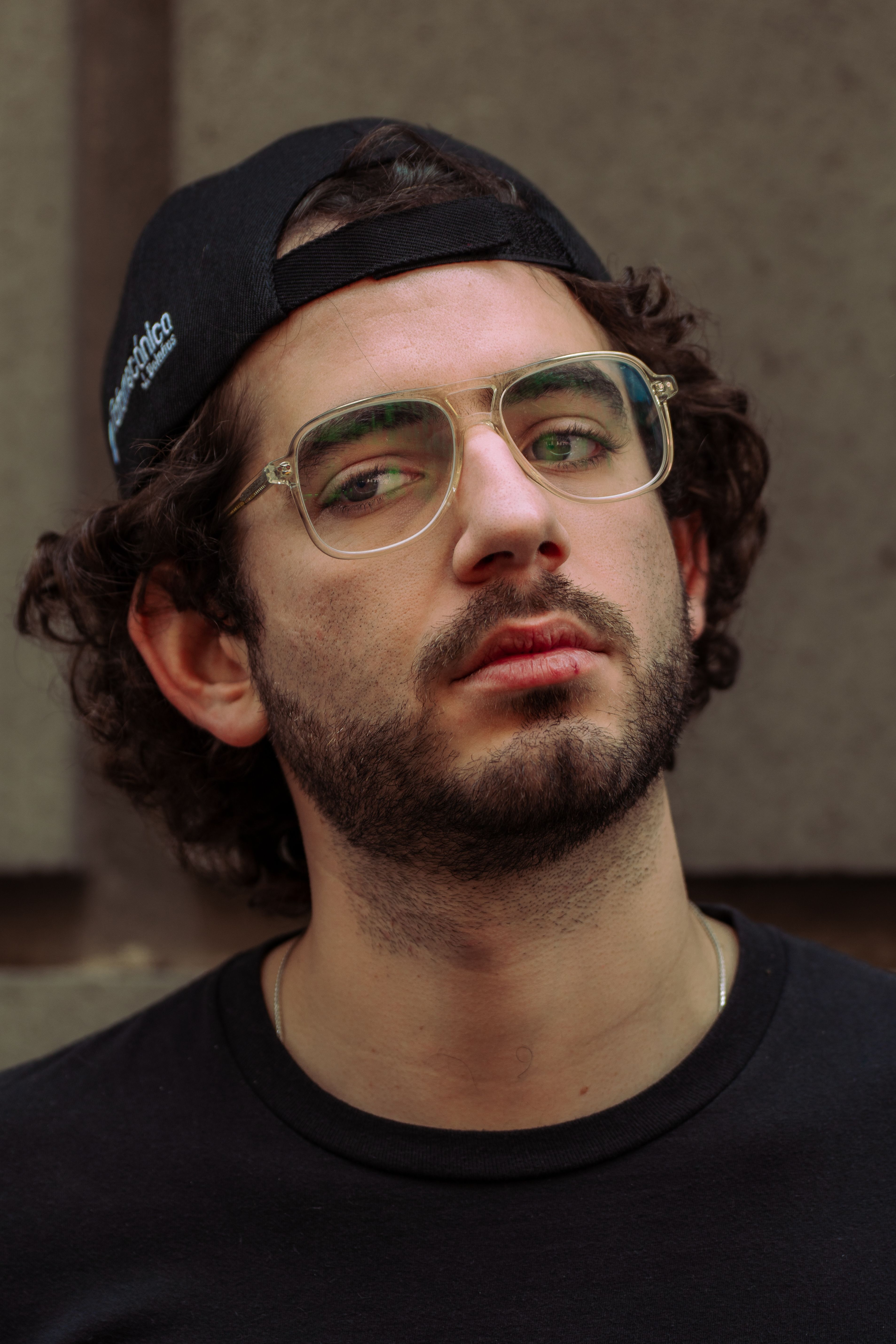 Close-up portrait of a man wearing eyeglasses and a cap, staring intently.