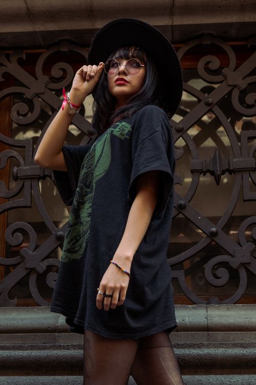 Free Stylish woman in oversized t-shirt and hat posing outdoors against ornate background. Stock Photo