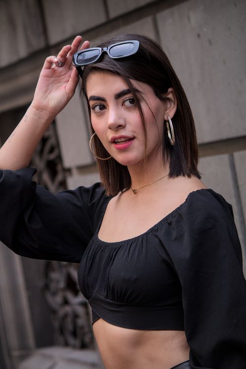 Free Portrait of a fashionable young adult woman wearing a black crop top and sunglasses outdoors. Stock Photo