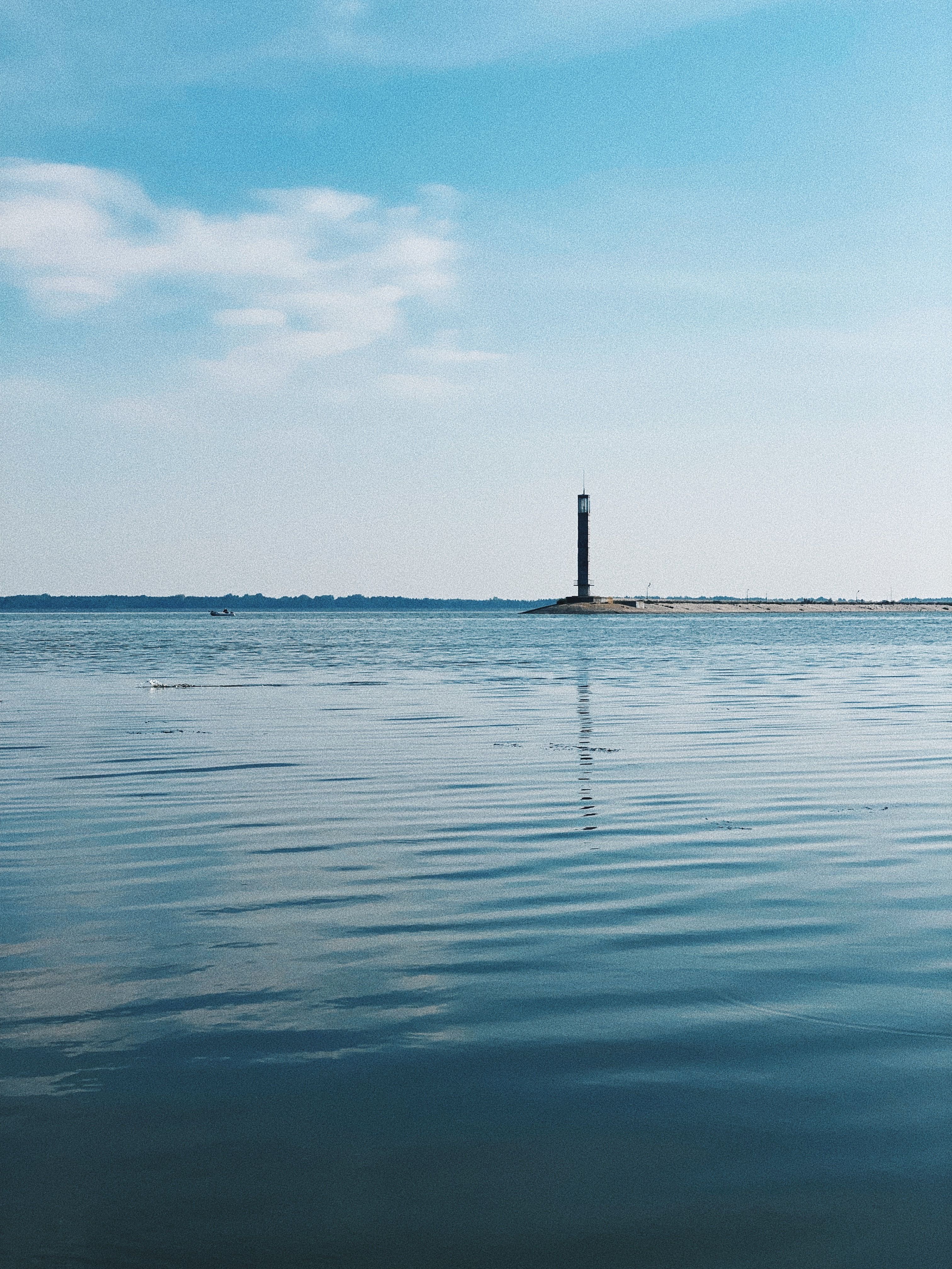 A solitary lighthouse stands against a tranquil ocean under a blue sky, reflecting serenity.