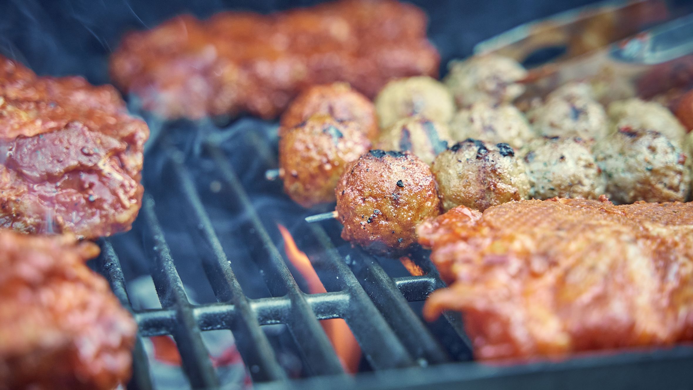 Delicious grilled meat and meatballs sizzling on an outdoor barbecue grill. Perfect for summer cookouts.