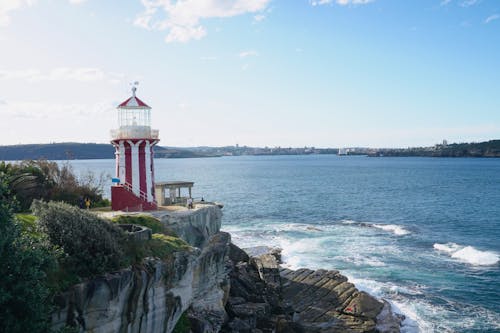 Red and White Lighthouse on Rock Formation Near Body of Water