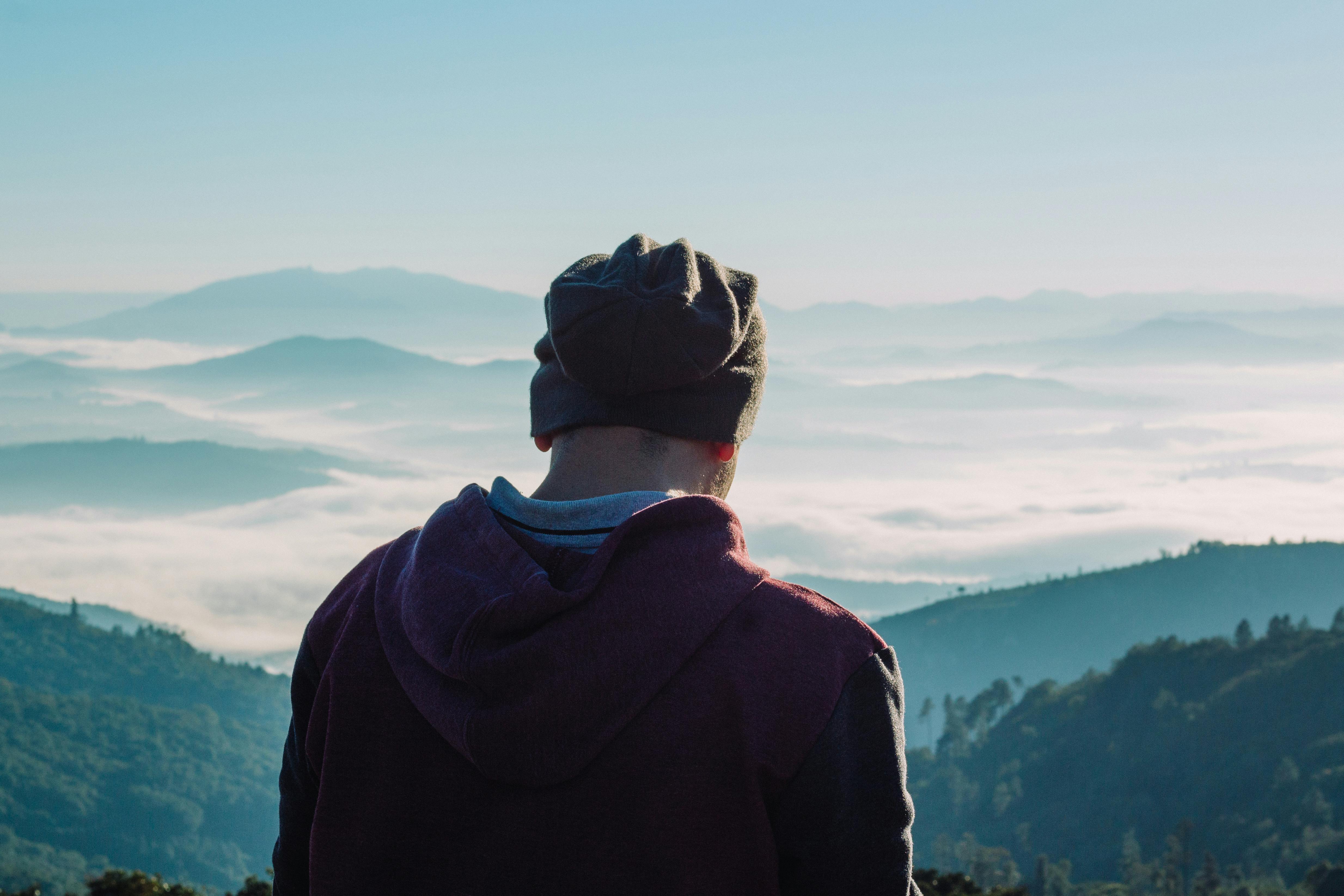 一位戴着无檐帽的男子，正欣赏云雾缭绕的静谧山景