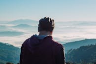 一位戴着无檐帽的男子，正欣赏云雾缭绕的静谧山景